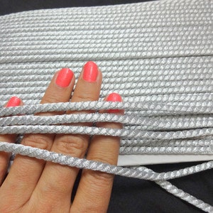 May include: Silver cord trim with a textured surface. The cord is approximately 1/4 inch wide.