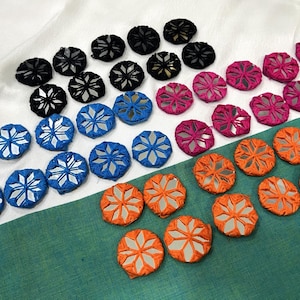 Peut inclure: Une collection de patchs en tissu circulaires dotés d'une incrustation miroir en forme d'étoile au centre. Les patchs sont disposés en groupes noirs, bleus, roses et orange, chacun présentant un motif géométrique cousu autour du centre réfléchissant.