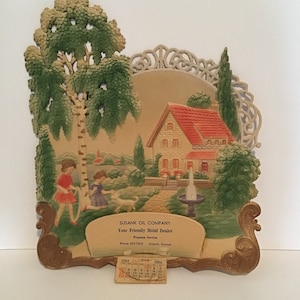 May include: A vintage calendar featuring a charming illustration of a house with a red roof, a fountain, and two children in a garden setting. The calendar is for January 1963 and is from the Susank Oil Company, a Mobil dealer offering propane service.