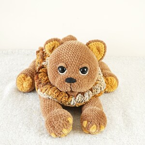 May include: A brown crocheted lion plush toy with a yellow and brown mane. The lion has black eyes and a black nose.