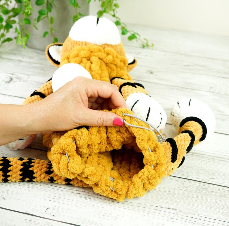 May include: A crocheted tiger stuffed animal with orange and black stripes. The tiger is being sewn together with safety pins.