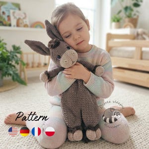 May include: A handmade, crocheted donkey plush toy in shades of brown and tan is held by a person. The donkey has long ears, a fluffy mane, and a sweet expression. The word "Pattern" is visible in the image.