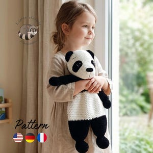 Könnte beinhalten: Ein handgefertigtes Häkel-Panda-Schmusetuch mit weißem Kopf, schwarzen Augenpartien, schwarzen Ohren und schwarzen Gliedmaßen an einem weißen, strukturierten Körper. Das Spielzeug hat schwarze Sicherheitsaugen und eine gestickte Nase. Text Little sleepy Raccoon Pattern.