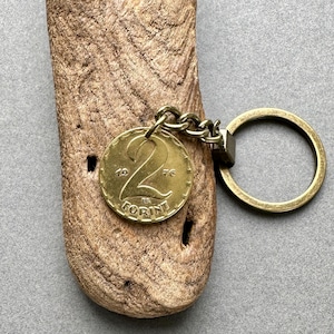May include: A vintage brass keychain featuring a 1976 Hungarian 2 Forint coin. The coin is attached to a chain and a round key ring. The keychain is displayed on a piece of weathered wood.