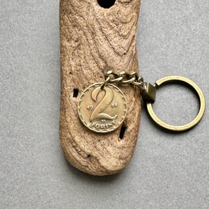 May include: A vintage-style keychain featuring a bronze coin with the number "2" and the text "FORINT" attached to a wooden piece. The keychain has a bronze-colored chain and key ring. The coin is dated 1933.
