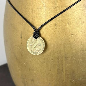 May include: A gold-colored coin pendant necklace. The coin features the number "2" and the word "Forint". The necklace has a black cord. The coin is dated 1936.
