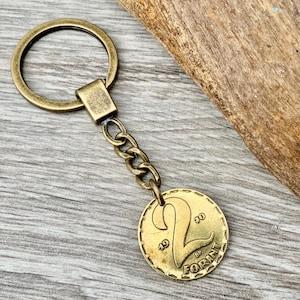 May include: Vintage brass keychain featuring a Hungarian 2 Forint coin from 1930. The coin is attached to a chain and a brass key ring. The keychain is a unique accessory.