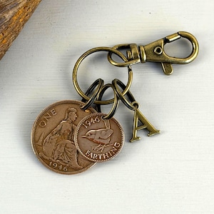 May include: Bronze-coloured keychain with two vintage coins and a letter "A" charm. The coins are attached to a keyring with a lobster clasp. One coin reads "ONE" and the other reads "1946 FARTHING".