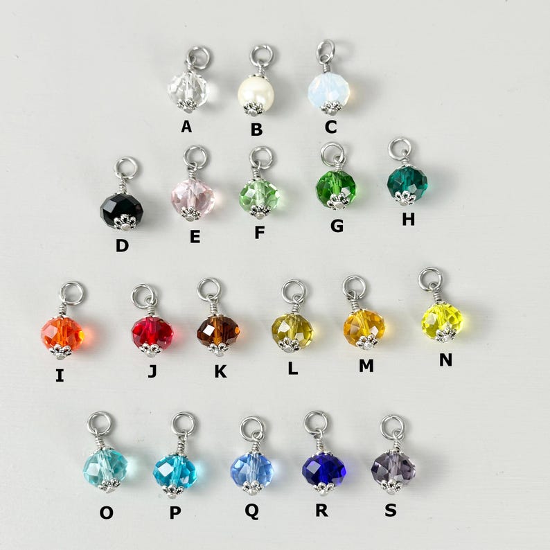 May include: A collection of sixteen colorful crystal charms with silver-tone metal findings. The charms are in various colors, including clear, white, pink, green, orange, red, brown, yellow, blue, and purple. Each charm has a unique shape and sparkle.