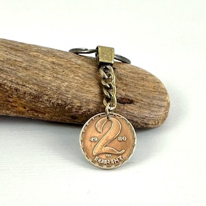 May include: A vintage coin keychain featuring a copper-colored coin with the number "2" prominently displayed. The coin is inscribed with "19" and "80" on either side of the number, and "FORINT" below. The keychain has a brass-colored chain and key ring.