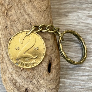 May include: A vintage gold-toned coin keychain. The coin features the number 2, the year 1970, and the word "FORINT" in a circular design. The keychain includes a chain and a textured key ring.