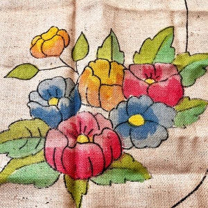 May include: A burlap fabric with a painted floral design. The flowers are in shades of red, blue, yellow, and orange. The leaves are green.