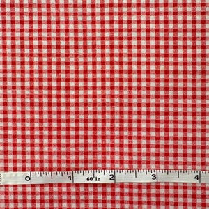 May include: Red and white gingham fabric with a measuring tape showing 60 inches. The fabric has a classic checkered pattern, with evenly spaced red and white squares. The measuring tape is white with black markings.