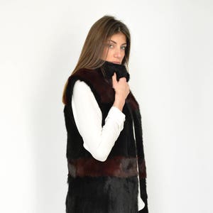Peut inclure: Un gilet en fourrure noir et marron avec un col montant. Le gilet est sans manches et a une coupe longue et fluide.
