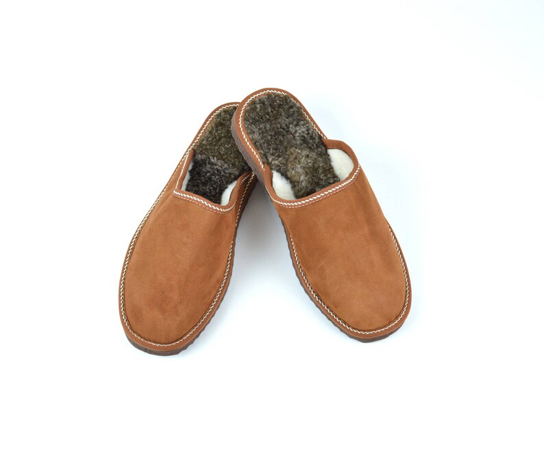 May include: A pair of brown suede slippers with a white trim and a fuzzy brown lining.
