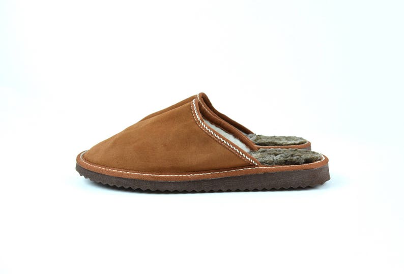 May include: Brown suede slippers with a white stitching detail and a brown fur lining.