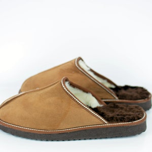 May include: A pair of brown suede slippers with a white sheepskin lining and a brown rubber sole.