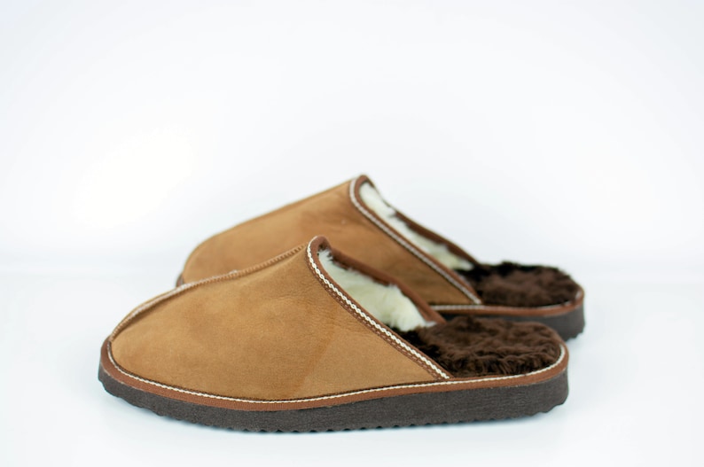 May include: A pair of brown suede slippers with a white sheepskin lining and a brown rubber sole.