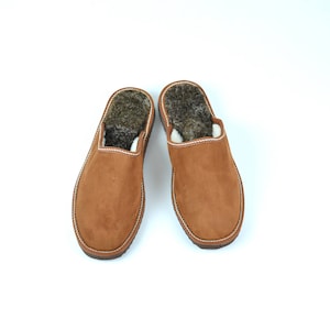 May include: A pair of brown suede slippers with a fluffy lining. The slippers have a closed toe and an open back.