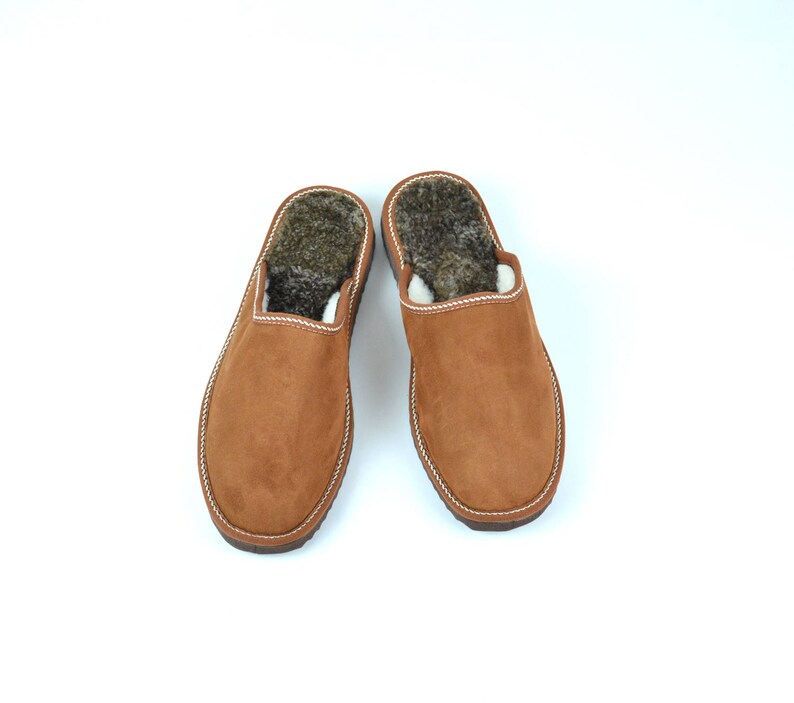 May include: A pair of brown suede slippers with a fluffy lining. The slippers have a closed toe and an open back.