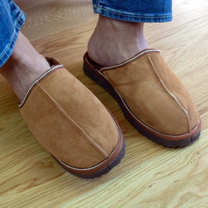 May include: A pair of brown suede slippers with white stitching and a brown rubber sole.