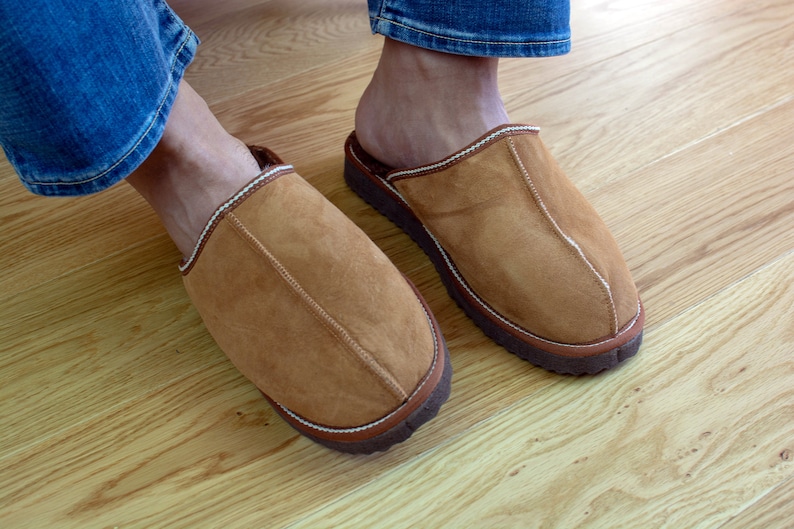 May include: A pair of brown suede slippers with white stitching and a brown rubber sole.