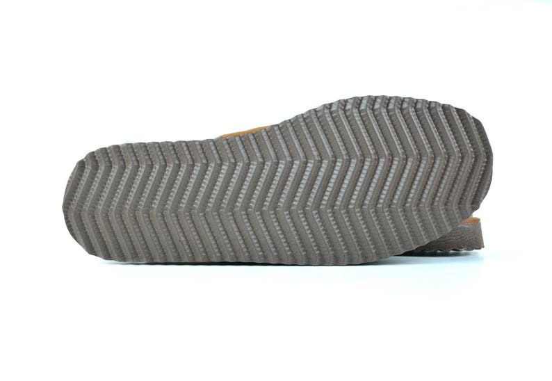 May include: Close-up of the bottom of a brown leather sandal with a textured rubber sole.
