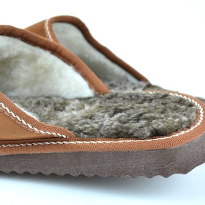 May include: A pair of brown leather slippers with a white sheepskin lining. The slippers have a brown suede exterior and a brown rubber sole.
