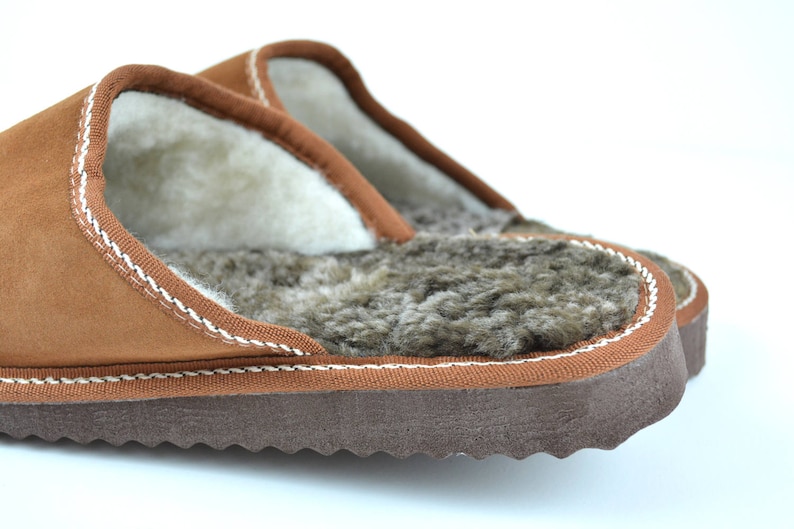 May include: A pair of brown leather slippers with a white sheepskin lining. The slippers have a brown suede exterior and a brown rubber sole.