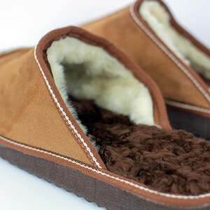May include: A pair of brown suede slippers with a white stitched trim and a brown faux fur lining.