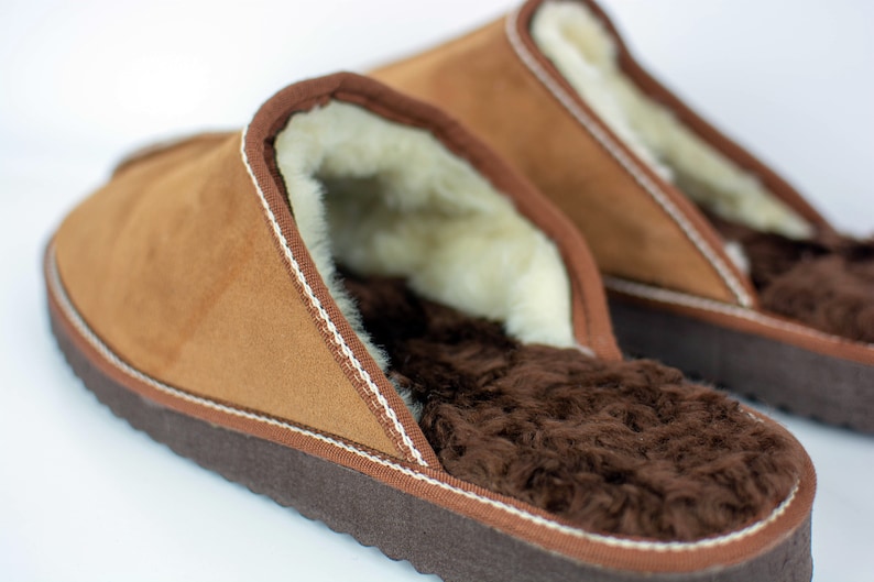 May include: A pair of brown suede slippers with a white stitched trim and a brown faux fur lining.