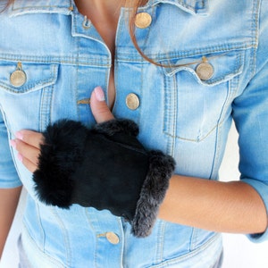 May include: Black faux fur and suede fingerless gloves with a denim jacket background.