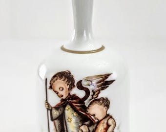 May include: White ceramic bell with a long handle and a detailed illustration of two children with angel wings. The bell has a gold trim and a classic design. A decorative item for collectors.