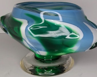 May include: A green, blue, and white glass bowl with a swirling pattern. The bowl is on a clear glass pedestal.
