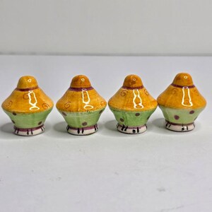 May include: Four ceramic mushroom-shaped figurines arranged in a row. Each piece features a rounded orange cap with brown swirl patterns, a light green base with dark purple polka dots, and a thin purple band separating the cap from the base.