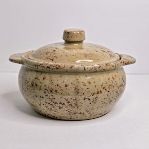 May include: A speckled beige ceramic casserole dish with a lid. The dish has a round shape with two small handles on either side and a knob on the lid. The dish is approximately 6 inches in diameter.