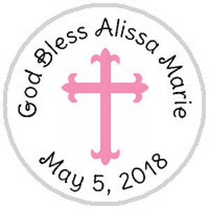 May include: A white circle with a gray border, featuring a pink cross with decorative flourishes. The text "God Bless Alissa Marie May 5, 2018" is written around the cross.