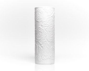 May include: A tall, white ceramic vase with a cylindrical shape. The vase is decorated with a repeating pattern of raised, swirling floral designs. The vase is approximately 12 inches tall and has a smooth, glossy finish. The background is white.