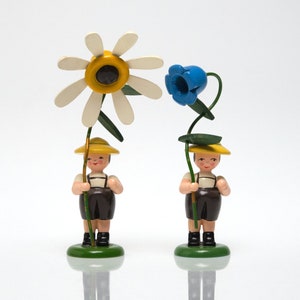 Könnte beinhalten: Zwei Holzfiguren von Kindern, die Blumen halten. Das Kind links hält eine weiße Margerite mit gelber Mitte. Das Kind rechts hält eine blaue Glockenblume. Beide Kinder tragen gelbe Hüte und braune Hosen.