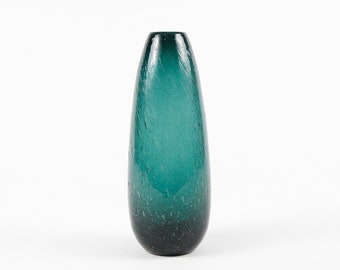 May include: A teal blue glass vase with a textured surface. The vase is tall and narrow, with a rounded bottom and a slightly flared opening.