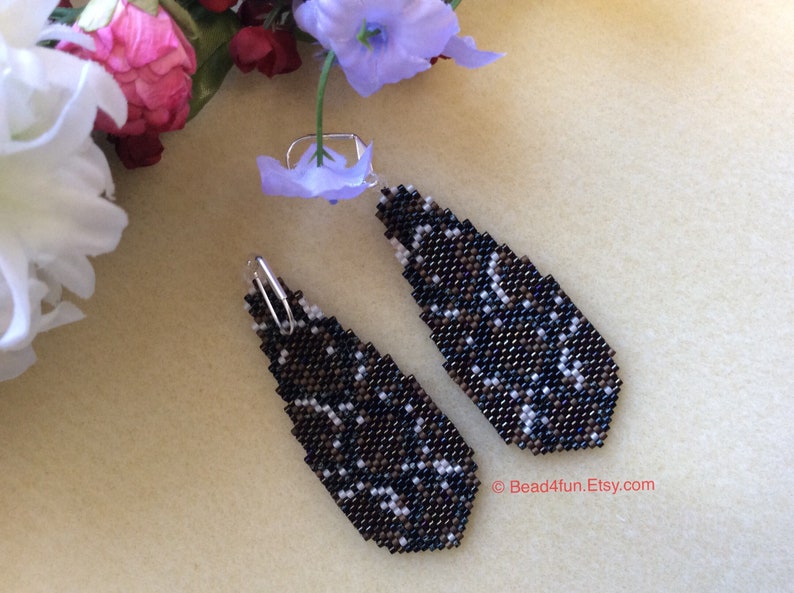 Peut inclure: Une paire de boucles d'oreilles pendantes avec un motif g&eacute;om&eacute;trique noir, brun et blanc. Les boucles d'oreilles sont faites de perles de rocaille et ont des crochets argent&eacute;s.