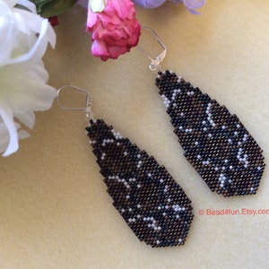 May include: A pair of long, teardrop-shaped earrings with a black, brown, and white beaded pattern. The earrings have silver hooks.