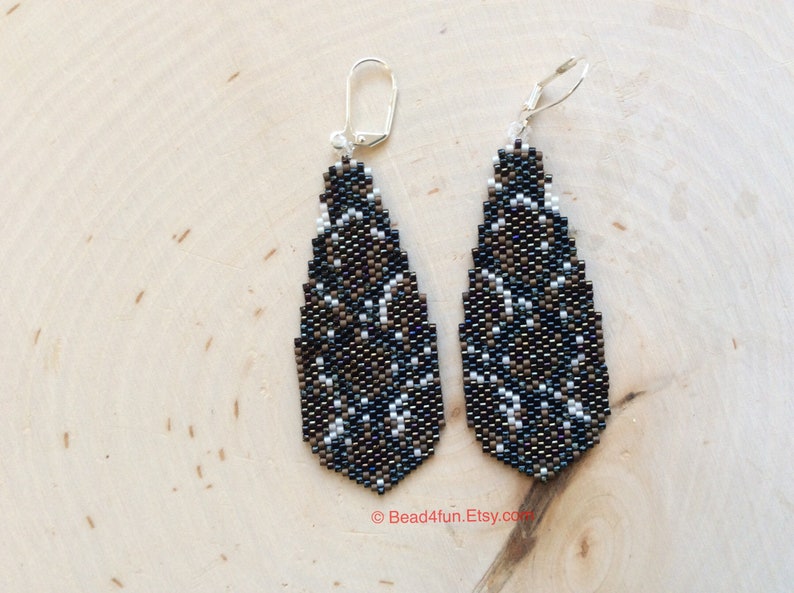 Peut inclure: Une paire de longues boucles d'oreilles en forme de goutte d'eau avec un motif g&eacute;om&eacute;trique noir, brun et blanc. Les boucles d'oreilles sont faites de perles de rocaille et ont des crochets argent&eacute;s.