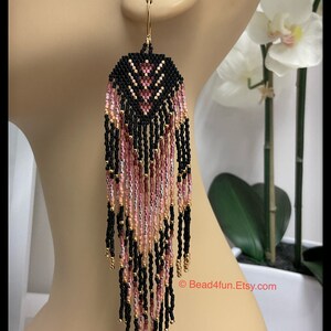 May include: Black and pink beaded earrings with a geometric pattern and gold accents. The earrings are long and dangle, with a fringe of beads at the bottom.