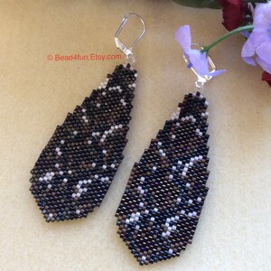 Peut inclure: Une paire de boucles d'oreilles pendantes de forme g&eacute;om&eacute;trique en goutte d'eau. Les boucles d'oreilles sont faites de perles noires et blanches et ont une fermeture &agrave; crochet argent&eacute;e.