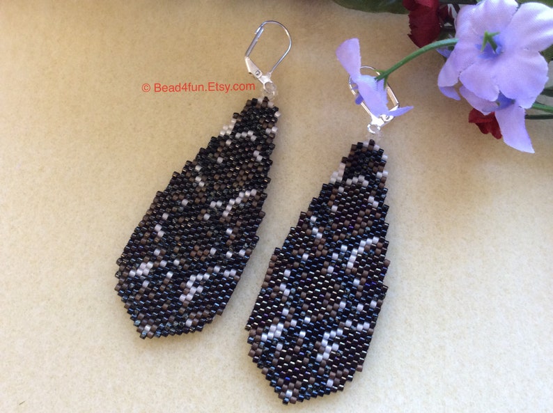 Peut inclure: Une paire de boucles d'oreilles pendantes de forme g&eacute;om&eacute;trique en goutte d'eau. Les boucles d'oreilles sont faites de perles noires et blanches et ont une fermeture &agrave; crochet argent&eacute;e.