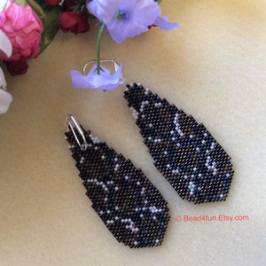 Peut inclure: Une paire de boucles d'oreilles pendantes avec un motif g&eacute;om&eacute;trique noir, brun et blanc. Les boucles d'oreilles sont faites de perles de rocaille et ont des crochets argent&eacute;s.