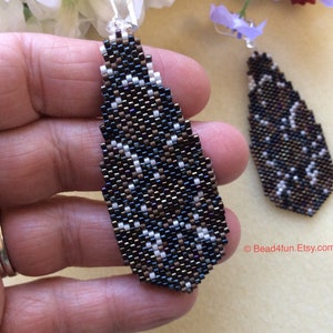 Peut inclure: Une paire de boucles d'oreilles pendantes en forme de larme. Les boucles d'oreilles sont faites de perles noires, brunes et blanches. Les perles sont dispos&eacute;es en un motif g&eacute;om&eacute;trique. Les boucles d'oreilles mesurent environ 5 cm de long.