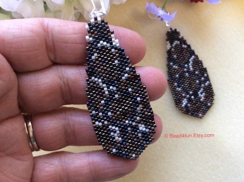 Peut inclure: Une paire de boucles d'oreilles pendantes en forme de larme. Les boucles d'oreilles sont faites de perles noires, brunes et blanches. Les perles sont dispos&eacute;es en un motif g&eacute;om&eacute;trique. Les boucles d'oreilles mesurent environ 5 cm de long.