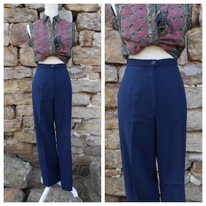 May include: Navy blue high-waisted trousers with a button closure. The pants are paired with a patterned sleeveless top. The outfit is displayed on a white mannequin against a stone wall background. The trousers have a classic, tailored fit.